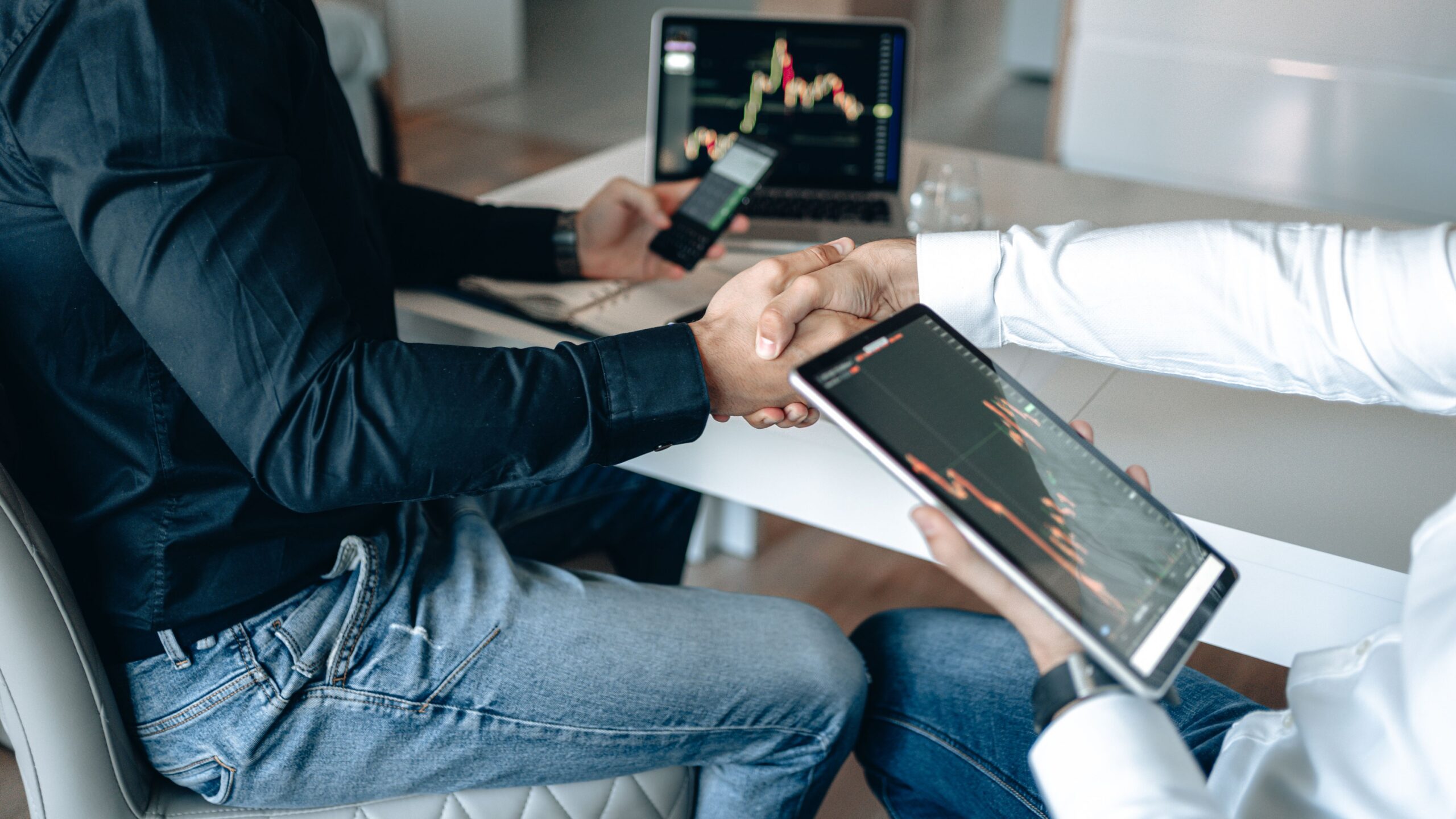 Two Digital Growth Partners shaking hands with financial graphs on digital devices.